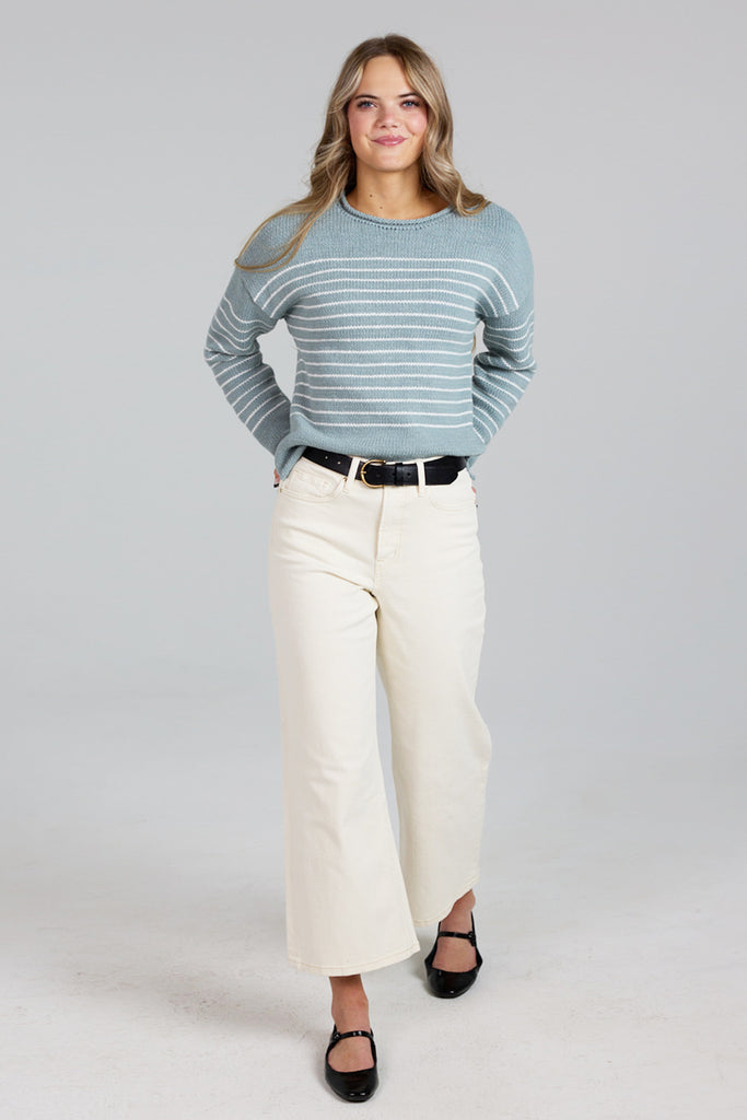 Model wearing a light blue with white stripes, logn sleeve, rolled round neck, dropped sleeve pullover sweater.