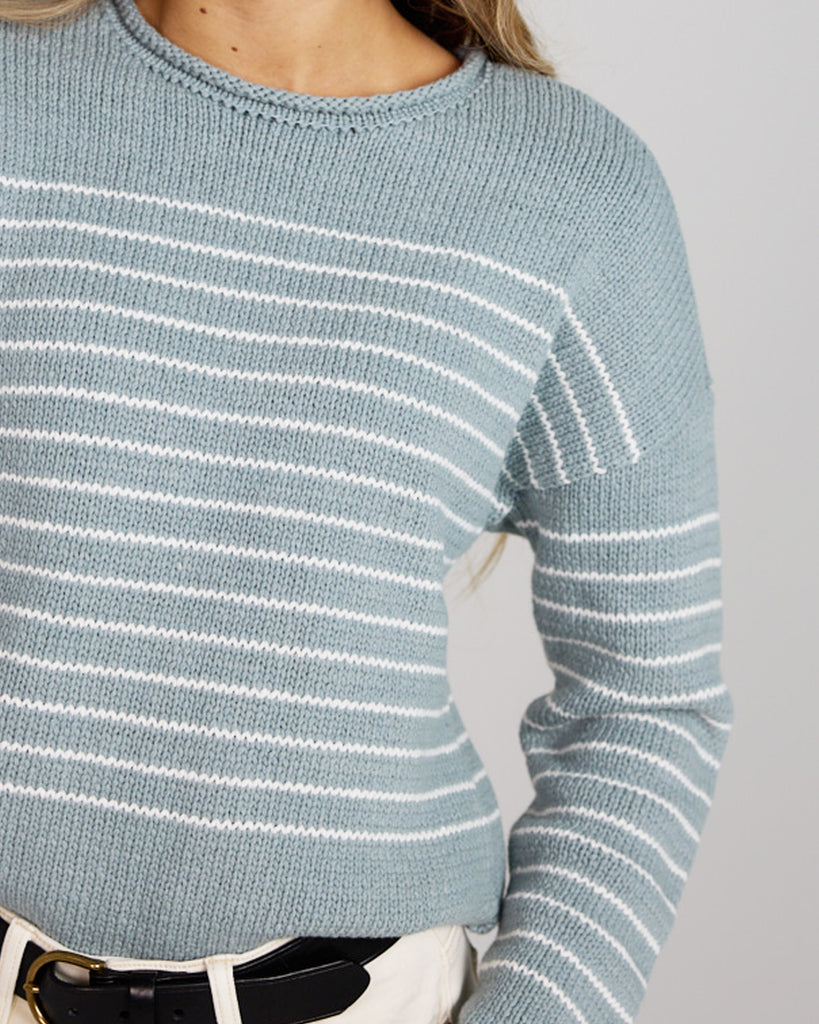 Model wearing a light blue with white stripes, logn sleeve, rolled round neck, dropped sleeve pullover sweater.