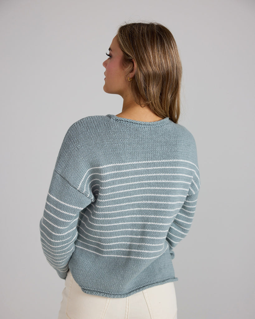 Model wearing a light blue with white stripes, logn sleeve, rolled round neck, dropped sleeve pullover sweater.