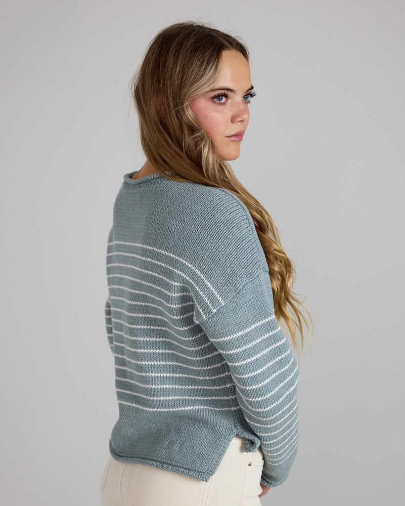 Model wearing a light blue with white stripes, logn sleeve, rolled round neck, dropped sleeve pullover sweater.