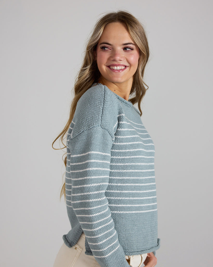 Model wearing a light blue with white stripes, logn sleeve, rolled round neck, dropped sleeve pullover sweater.