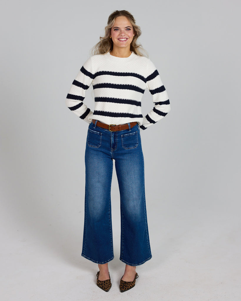 Model wearing a white with navy stripes long sleeve crew neck pullover sweater.