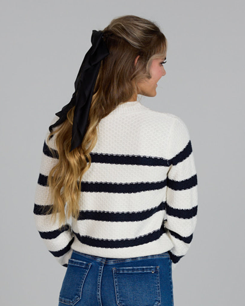 Model wearing a white with navy stripes long sleeve crew neck pullover sweater.