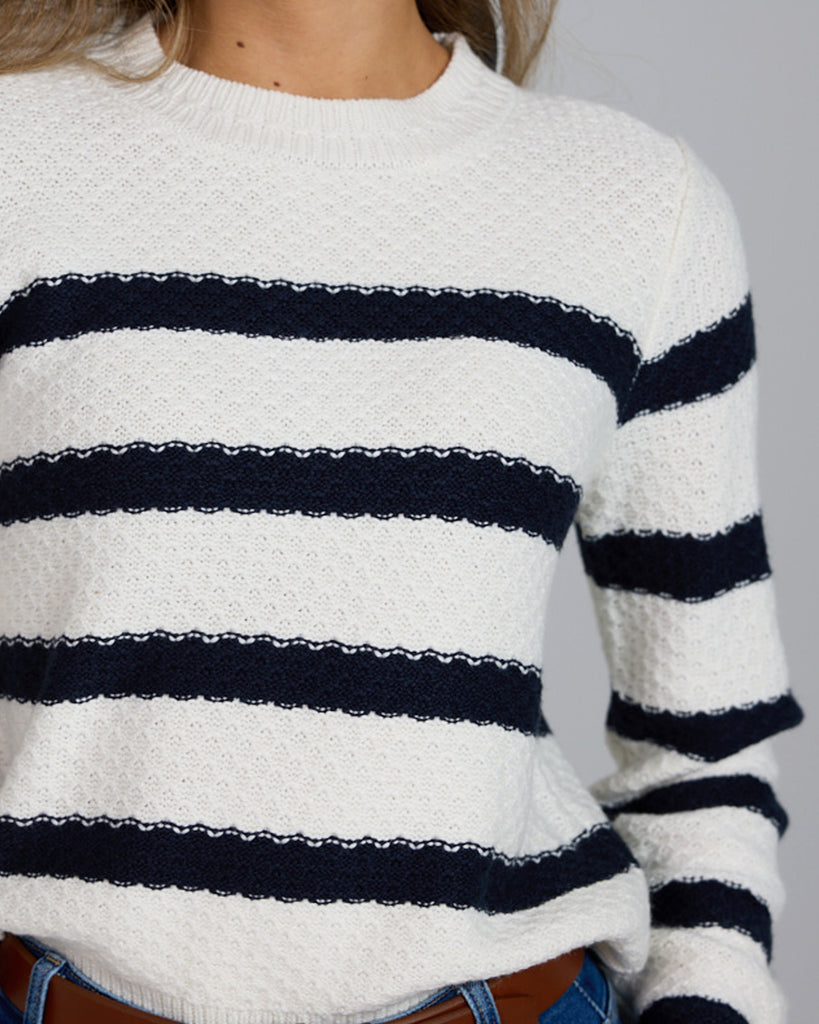 Model wearing a white with navy stripes long sleeve crew neck pullover sweater.