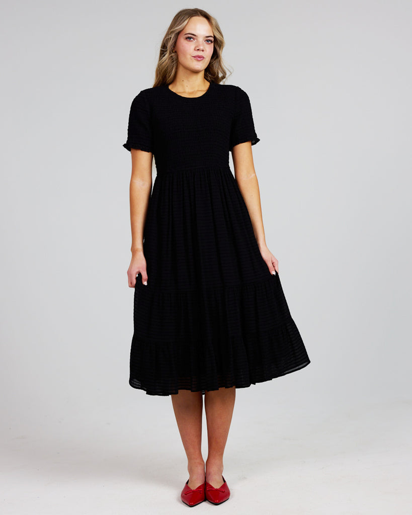 Model wearing a black short sleeve, round neck, midi length dress with a smocked bodice.