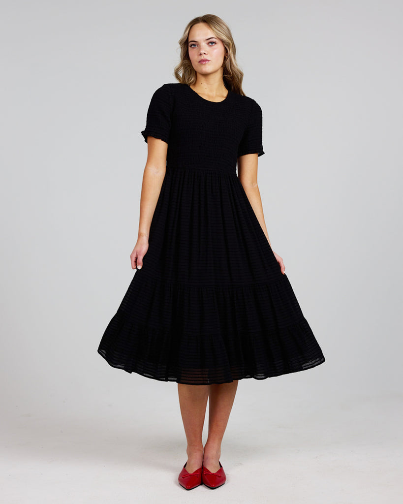 Model wearing a black short sleeve, round neck, midi length dress with a smocked bodice.