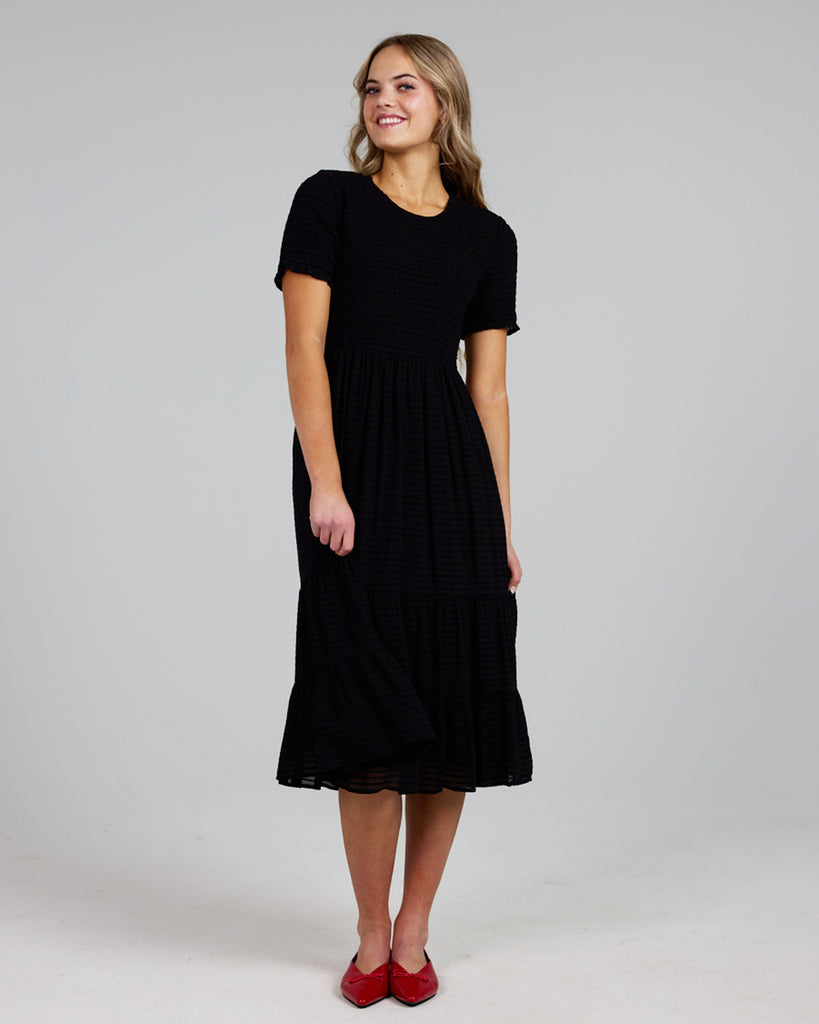 Model wearing a black short sleeve, round neck, midi length dress with a smocked bodice.