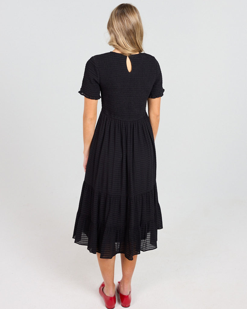 Model wearing a black short sleeve, round neck, midi length dress with a smocked bodice.