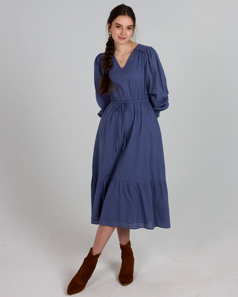 Model wearing a blue long sleeve, midi-length, v-neck dress.