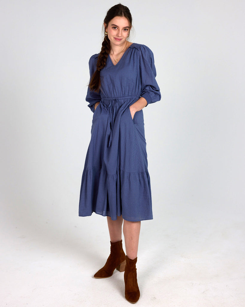 Model wearing a blue long sleeve, midi-length, v-neck dress with pockets.