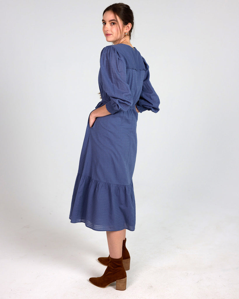 Model wearing a blue long sleeve, midi-length, v-neck dress.