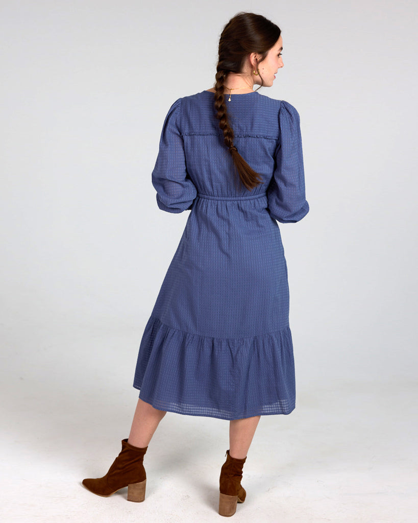 Model wearing a blue long sleeve, midi-length, v-neck dress.