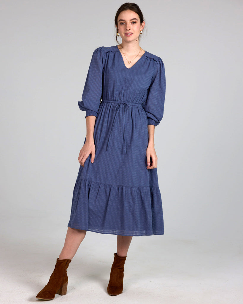 Model wearing a blue long sleeve, midi-length, v-neck dress.