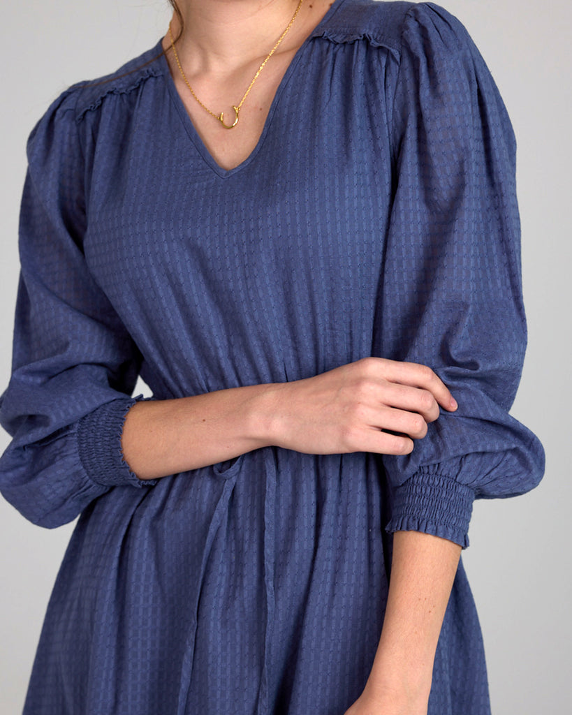 Model wearing a blue long sleeve, midi-length, v-neck dress.