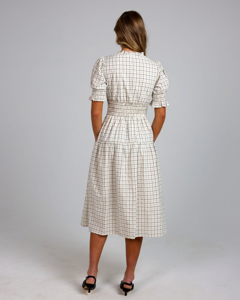 Model wearing a white and grey plaid short sleeve mock neck midi-length dress with smocking details around waist.