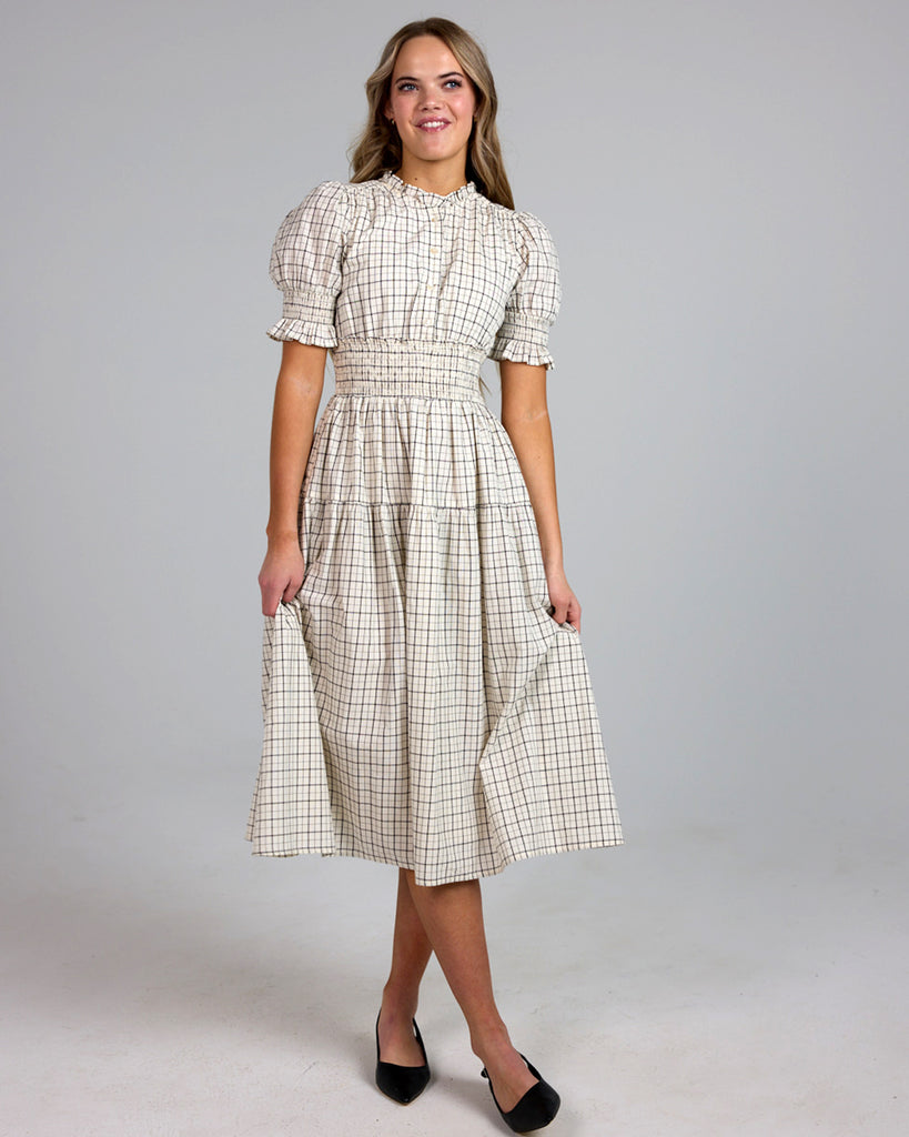 Model wearing a white and grey plaid short sleeve mock neck midi-length dress with smocking details around waist.