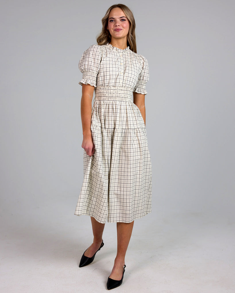 Model wearing a white and grey plaid short sleeve mock neck midi-length dress with smocking details around waist.