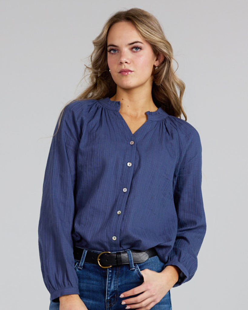 Model wearing a cobalt blue long sleeve v-neck blouse with button details down the front.