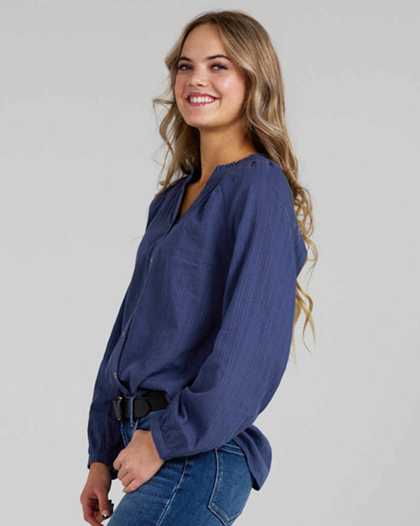 Model wearing a cobalt blue long sleeve v-neck blouse with button details down the front.