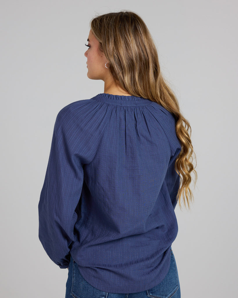 Model wearing a cobalt blue long sleeve v-neck blouse with button details down the front.