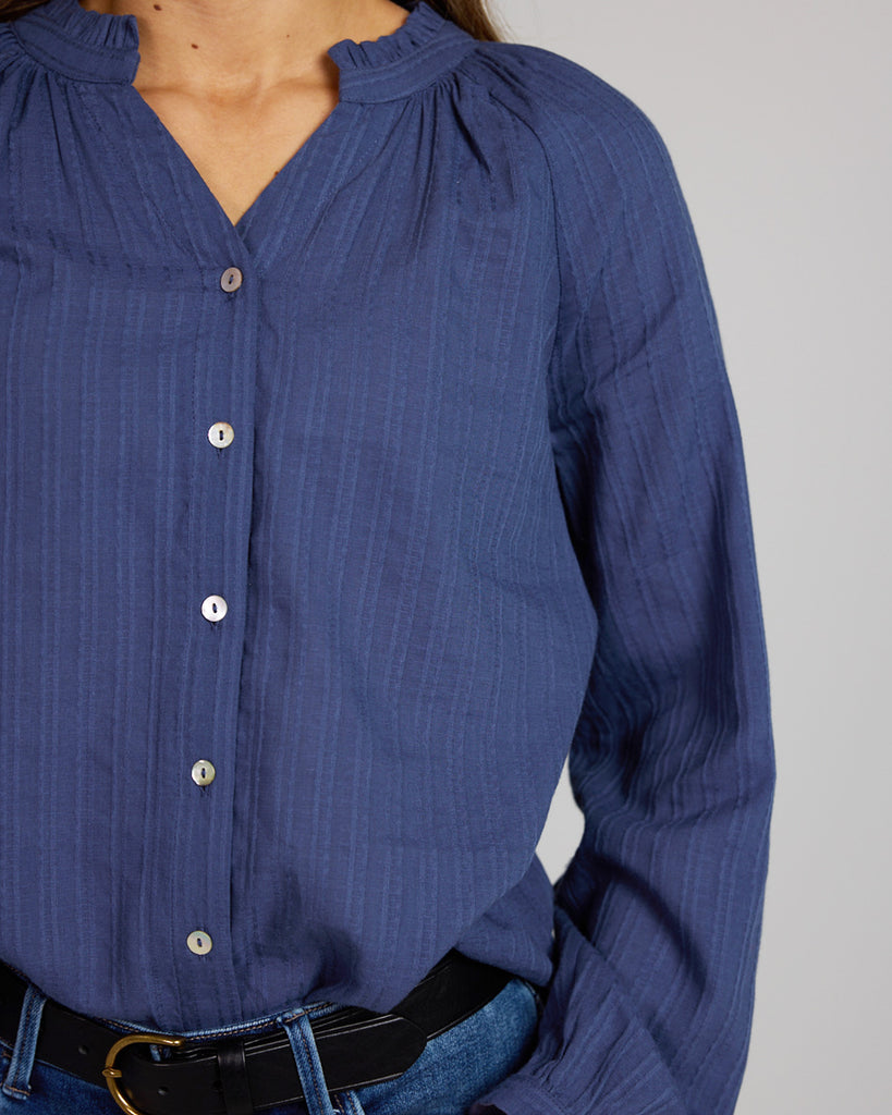 Model wearing a cobalt blue long sleeve v-neck blouse with button details down the front.