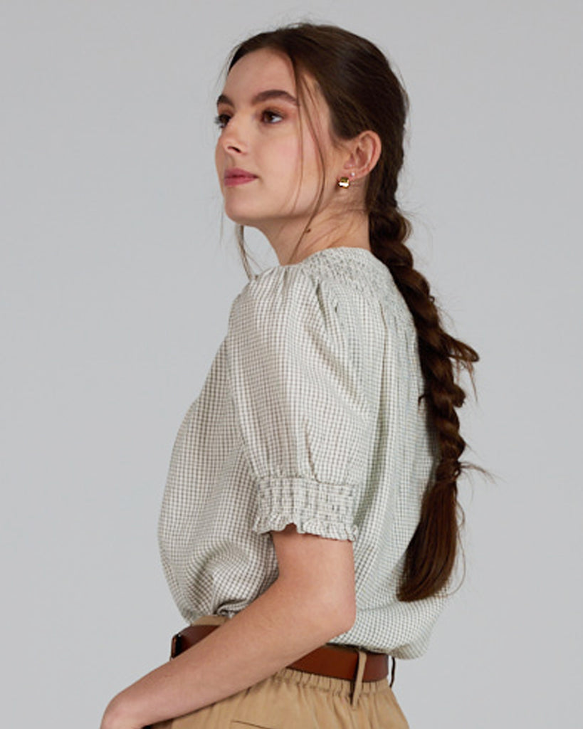 Model wearing a beige short sleeve blouse with button details and a small plaid pattern.