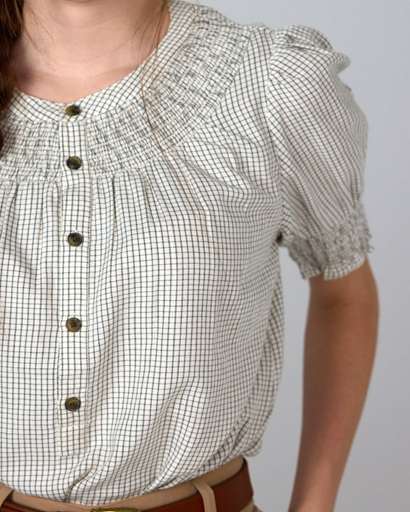 Model wearing a beige short sleeve blouse with button details and a small plaid pattern.