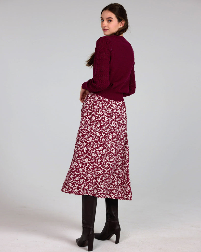 Model wearing a red with white flowers, midi-length, a-line skirt with buttons down the front.