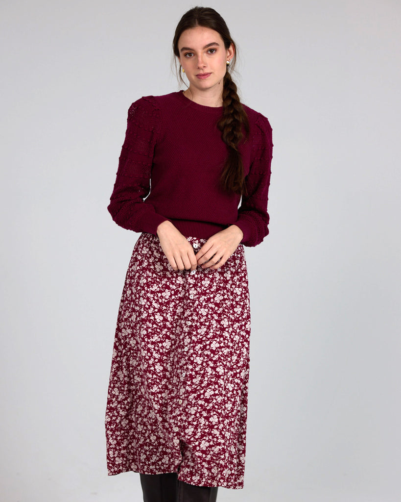 Model wearing a red with white flowers, midi-length, a-line skirt with buttons down the front.