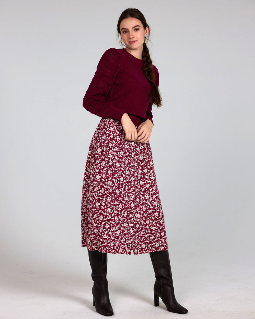 Model wearing a red with white flowers, midi-length, a-line skirt with buttons down the front.