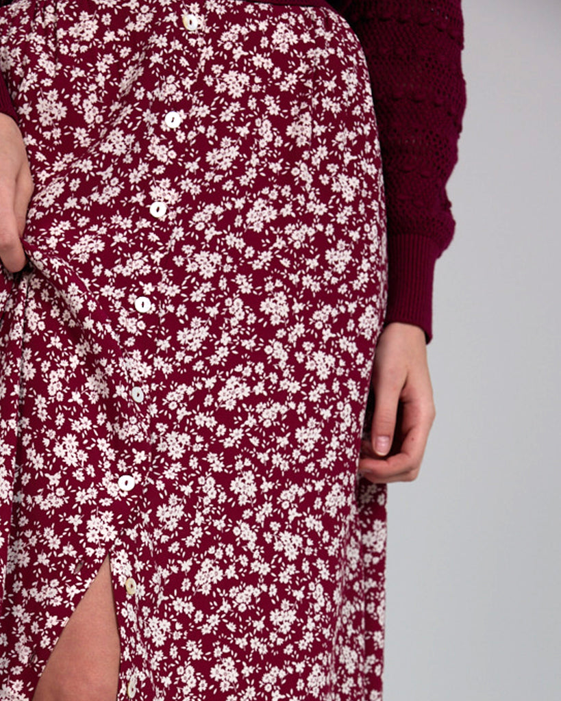 Model wearing a red with white flowers, midi-length, a-line skirt with buttons down the front.