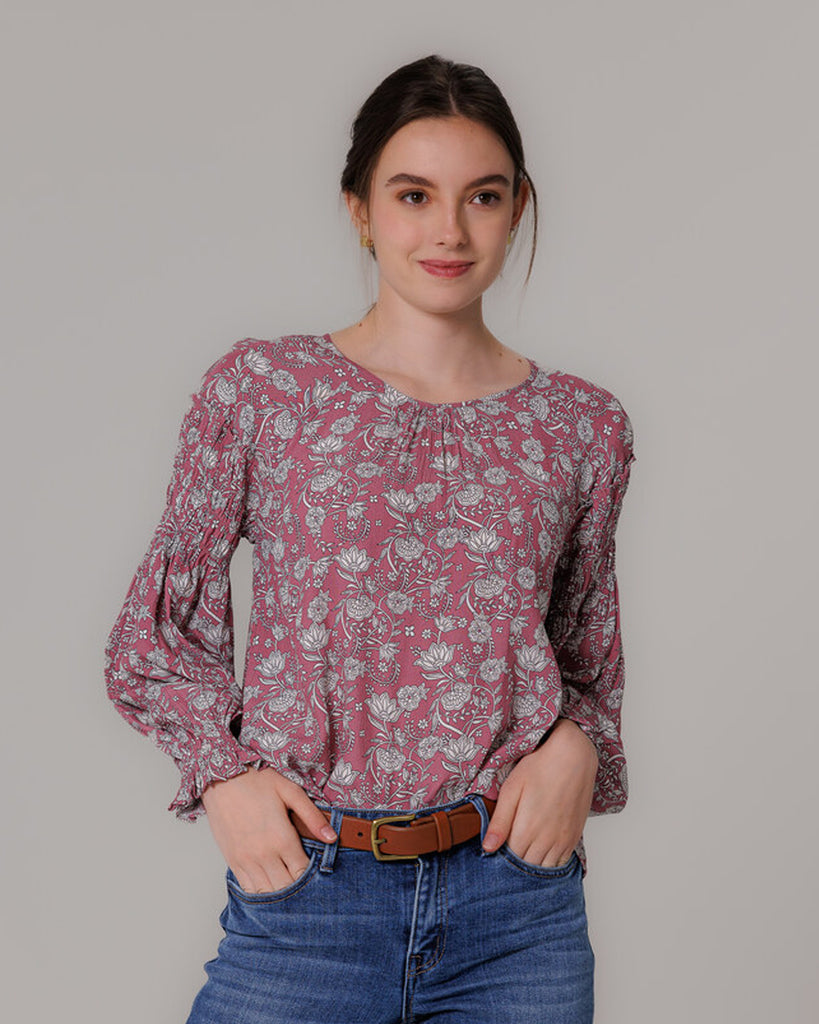 Model wearing a pink with grey floral print, long sleeve round neck blouse with shirring details on sleeve.