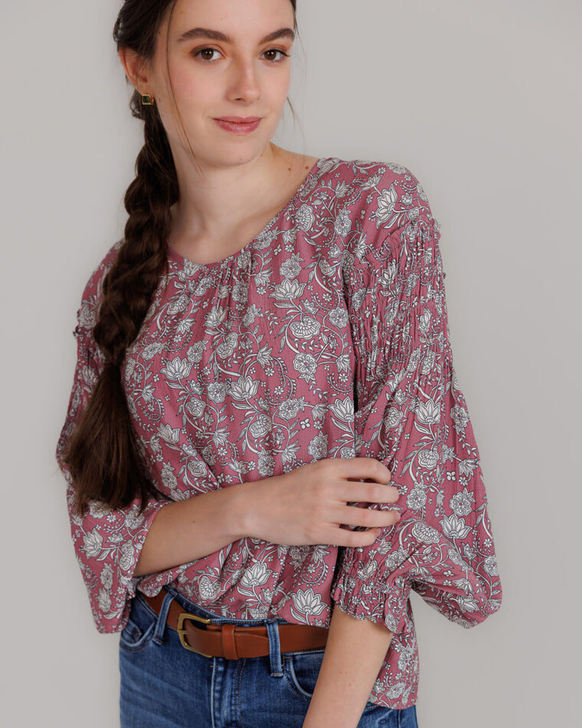 Model wearing a pink with grey floral print, long sleeve round neck blouse with shirring details on sleeve.