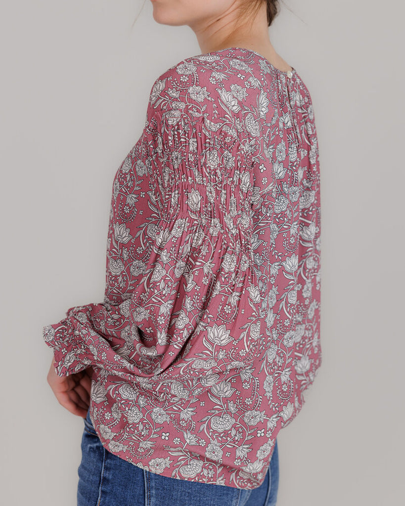 Model wearing a pink with grey floral print, long sleeve round neck blouse with shirring details on sleeve.