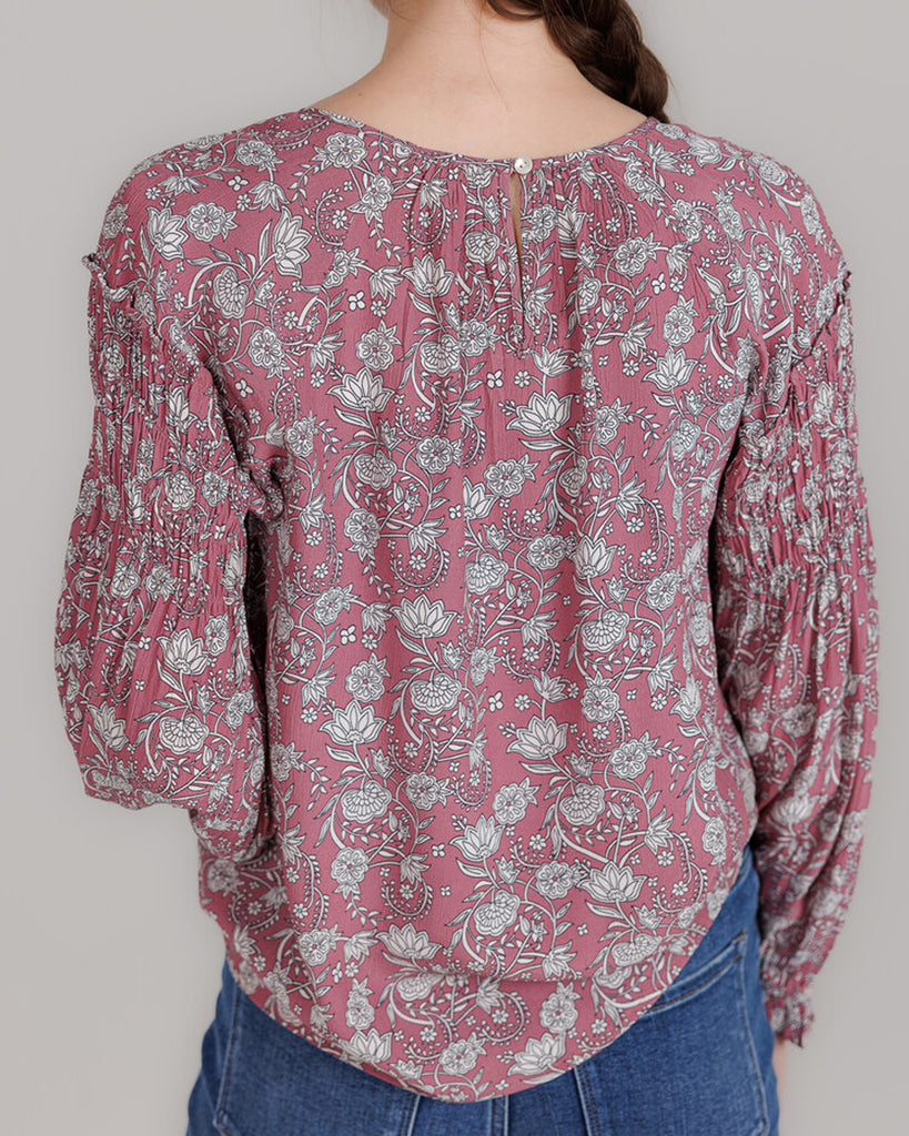 Model wearing a pink with grey floral print, long sleeve round neck blouse with shirring details on sleeve.