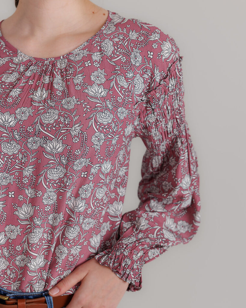 Model wearing a pink with grey floral print, long sleeve round neck blouse with shirring details on sleeve.