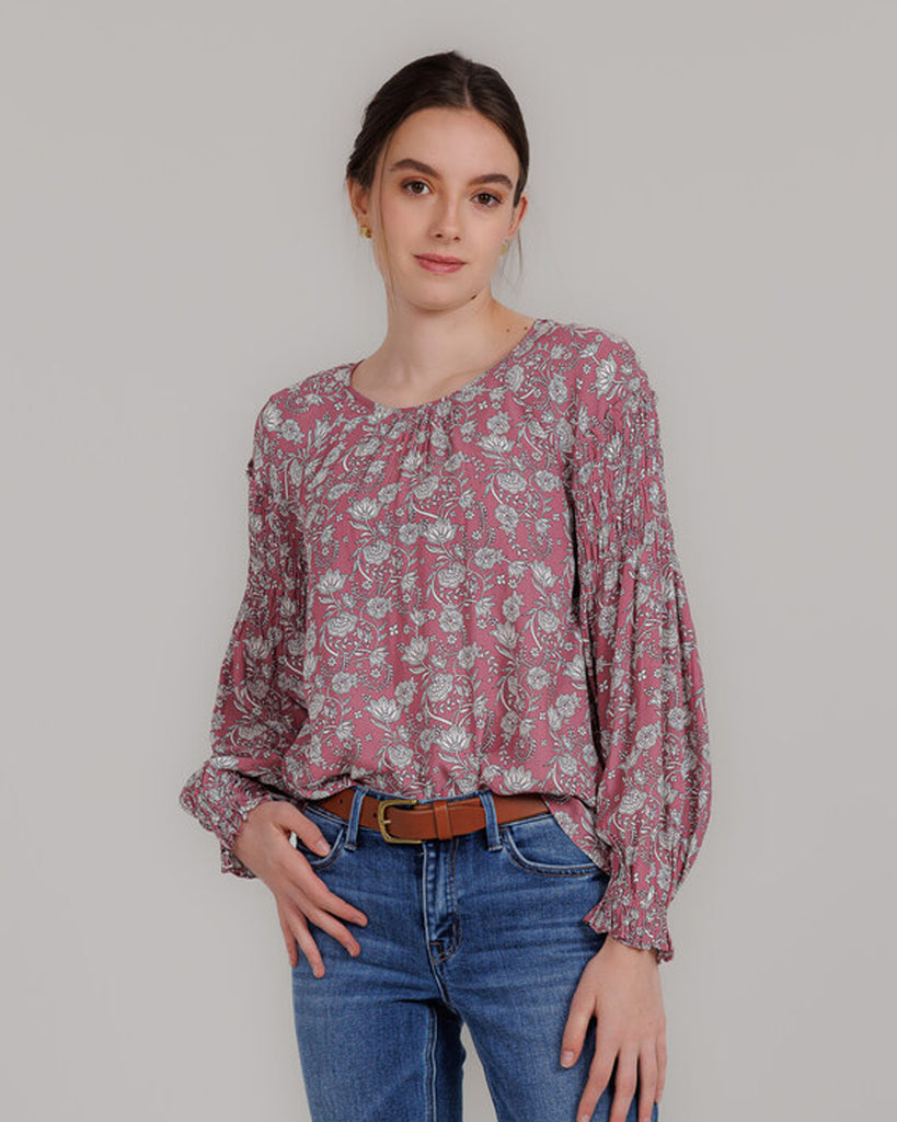 Model wearing a pink with grey floral print, long sleeve round neck blouse with shirring details on sleeve.