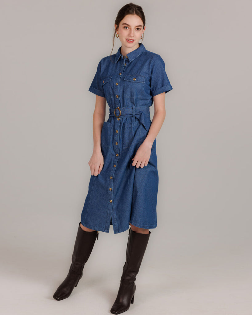 Model wearing a blue denim short sleeve, collared, knee-length dress with buttons down the front and a sash around the waist.