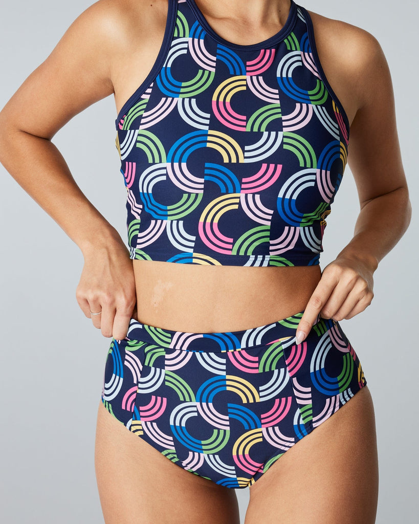 Woman in a two-piece swimsuit with a rainbow print and patterned top & bottom.