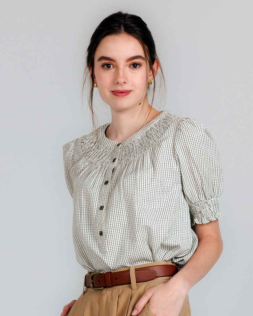 Model wearing a beige short sleeve blouse with button details and a small plaid pattern.