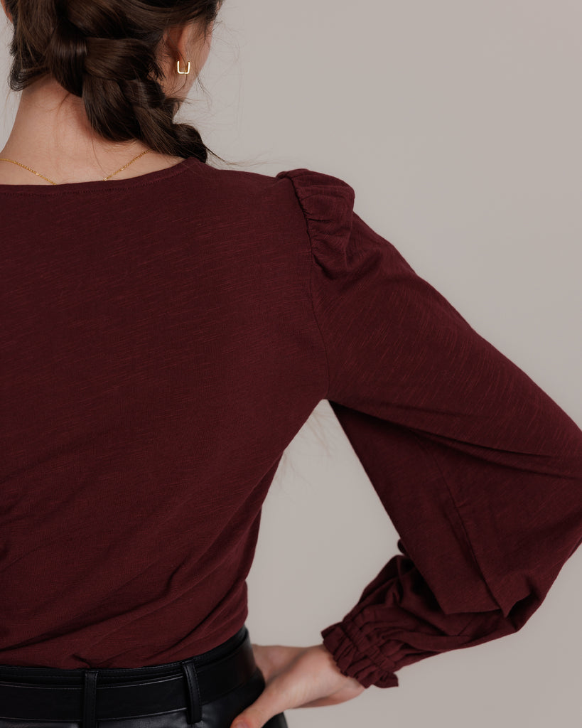 Model wearing a burgundy long balloon sleeve, v-neck knit top.